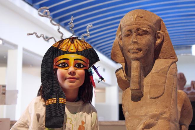enfant avec masque égyptien à côté d'une statue de sphinx égyptien